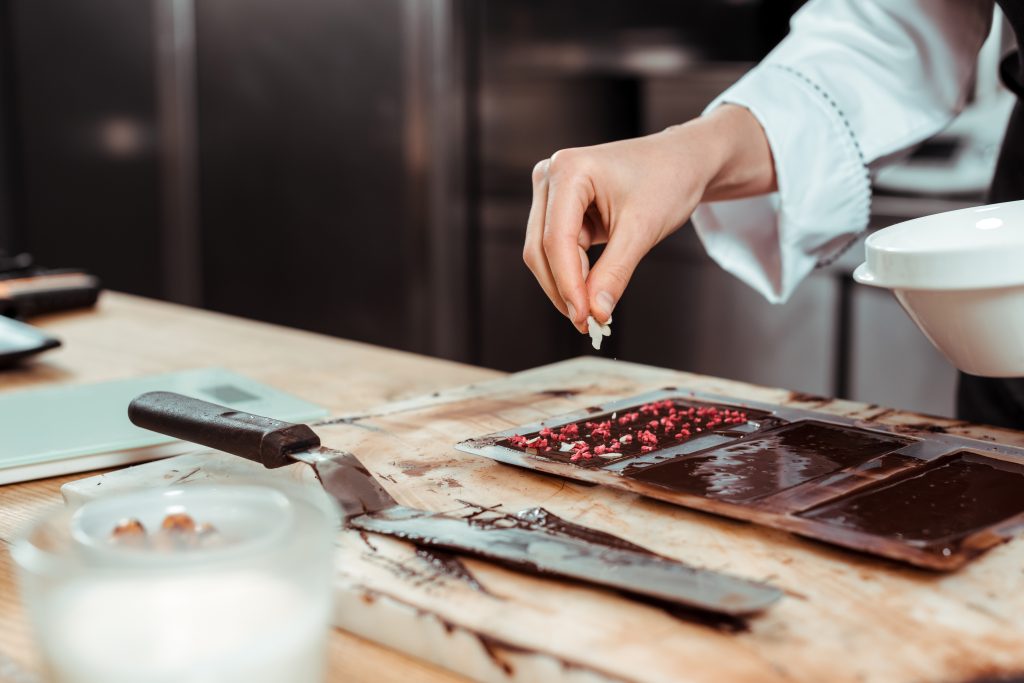 Cropped,View,Of,Chocolatier,Adding,Coconut,Flakes,On,Dark,Chocolate